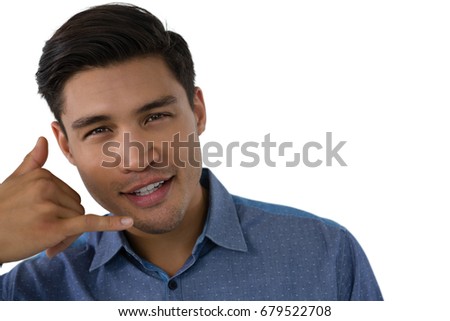 Portrait of young businessman gesturing call hand sign against white background