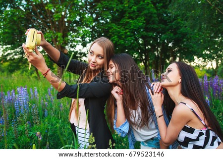 Three hipsters girls blonde and brunette taking self portrait on photo camera and smiling. Girls having fun together in park.