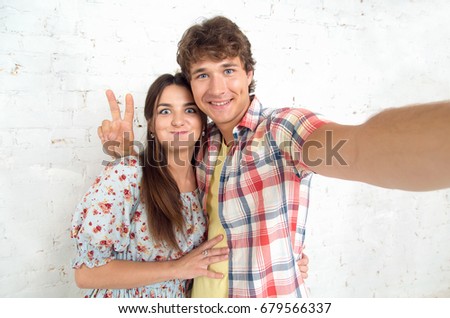 Selfie couple in love. Funny couple taking self portrait with smart phone. Beautiful young couple selfie. Students making selfie photo showing gesture V sign.