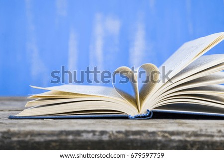 Open book on a wooden table on a blue background. Pages of the book in the form of a heart.
