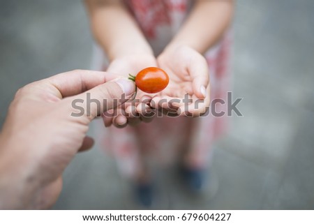Parent and child handing small tomato