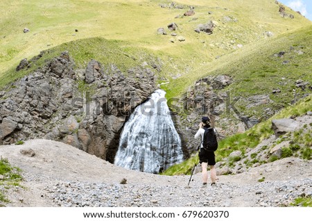 A beautiful mountain landscape. A girl is a tourist taking pictures of a mountain waterfall.