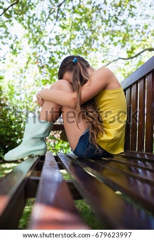 Side view of sad girl sitting on wooden bench at backyard