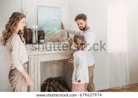 Happy family hanging picture of sea over the fireplace at home