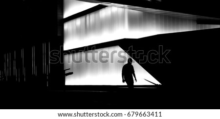 Silhouette of a man walking the city street stairs in front of modern building in central business district in late night hours