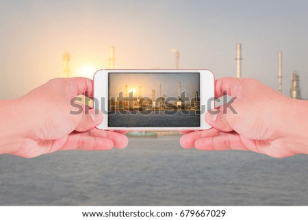 hand hold smartphone, cellphone to take a photo, oil fuel, Electric generating factory, plant near the river and sunset as industry, energy, communication and technology concept.
