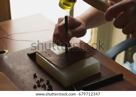 Woman is crafting on leather's work desk and strike hammer to awl on leather by handmade
