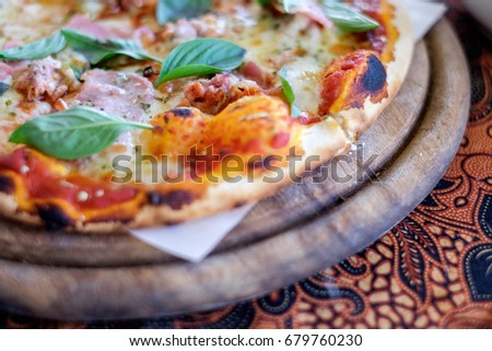 Closeup shot of slices of cheese pizza with dough crust, cheese, bacon, basil and pizza sauce on paper and wooden pan for concept of fast food. Selective blur effect.