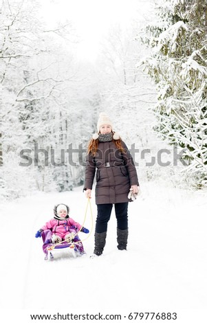 mother is towing daughter on the sledge in winter forest through the snow