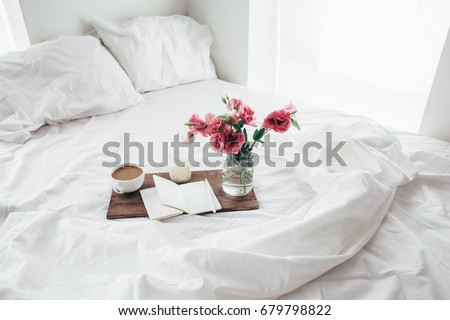 Wooden tray with paper sketchbook, candle and spring flowers on clean white bedding. Good morning concept.
