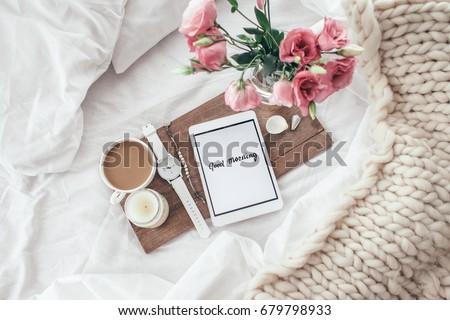Wooden tray with tablet, coffee and spring flowers on clean white bedding. Good morning concept.