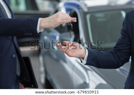 Cropped close up of a salesman handing over car keys to a new owner. Man receiving keys to his new car from a salesman at the dealership automotive industry salesperson seller selling buyer customer