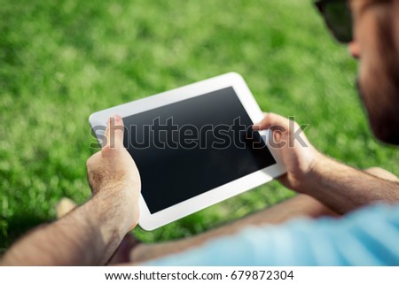 Young man using and typing tablet computer in summer grass.