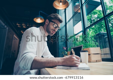 Yow angle view of a young stylish well dressed author writer is working in a modern coworking, writing the novel, in glasses, so serious and focused Royalty-Free Stock Photo #679913116