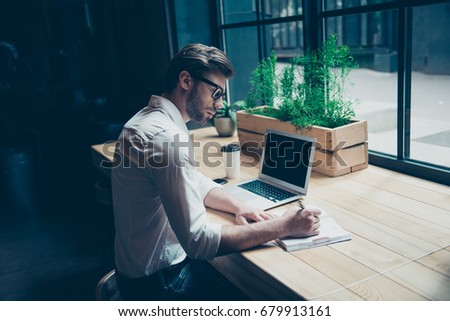 Rear view of a journalist stylish guy writing a story in a workplace in loft styled coworking, well dressed, in glasses Royalty-Free Stock Photo #679913161