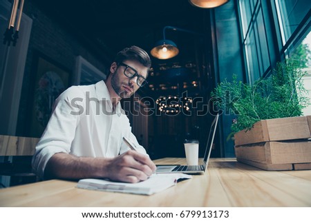 Young stylish well dressed author writer is working in a modern coworking, writing the novel, in glasses, so serious and focused Royalty-Free Stock Photo #679913173