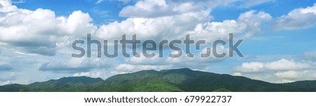 Blue sky panorama with clouds over tops of green mountain