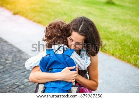 A woman hugs a curly-haired boy and smiles. Mom feels sorry for her son. Meeting mom and baby after separation. A child with a backpack hugs her mother. Royalty-Free Stock Photo #679967350