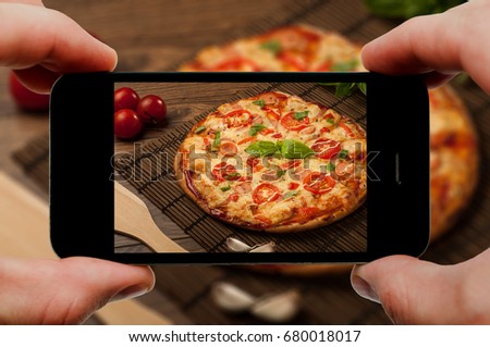 Taking photo of pizza by smartphone. Closeup view of process. File contains clipping paths for smartphone and hands and picture on it.