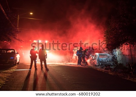 Firefighters and police officers extinguish a vehicle fire in the middle of the night.