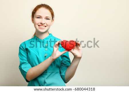Young nurse with heart in hands on neutral background