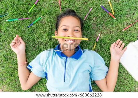 Asian girl playing with colored pencil,lying on grass 
