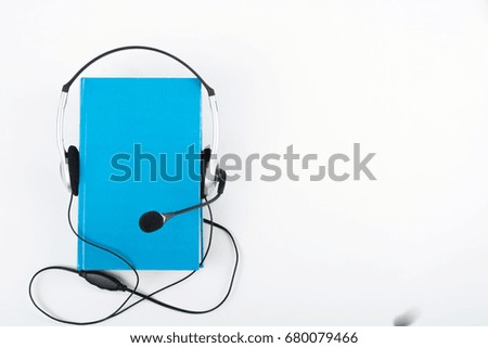 Audiobook on white background. Headphones put over blue hardback book, empty cover, copy space for ad text. Distance education, e-learning concept