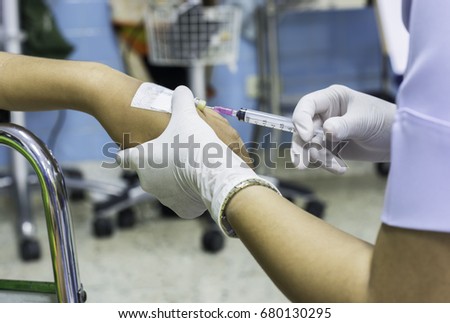 Woman in white shirt and gloves are injected into the vein through the injection plug for patients in a wheelchair at the hospital.