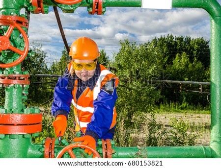 Woman worker in the oilfield repairing wellhead wearing orange helmet and work clothes. Industrial site background. Oil and gas concept.