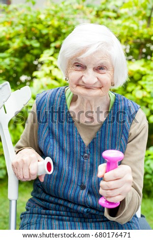 Picture of energized elderly woman doing sport exercises outdoor in the garden, holding pink dumbbells