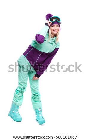 vertical picture, isolated on white, pretty caucasian woman in purple ski outfit, blue trousers and snow glasses, bend, hand on glasses, look at camera