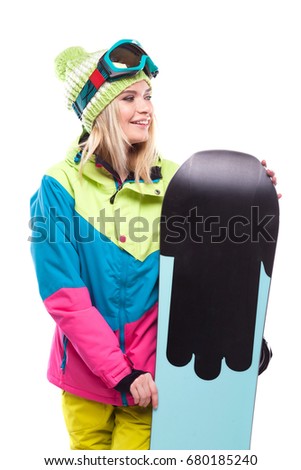 vertical picture, isolated on white, blonde pretty young caucasian woman in colorful ski outfit and blue snow goggles hold black snowboard, smiling