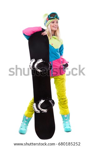 vertical picture, isolated on white, blonde pretty young caucasian woman in colorful ski outfit, yellow trousers and blue snow goggles hold black snowboard