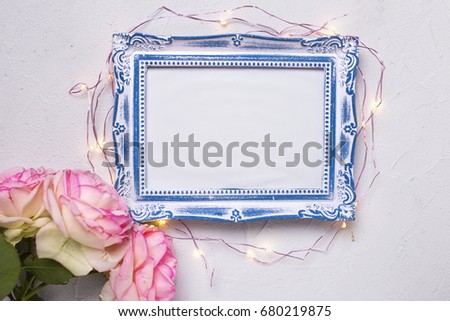 Empty photo frame, flowers  and fairy lights on grey textured background. Top view. Flat lay. Place for text. Mock up.