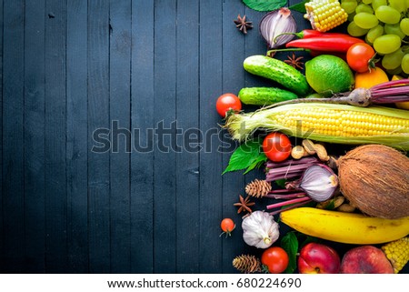 Large selection of raw vegetables and fruits on a black wooden table. Free space for your text. Top view.