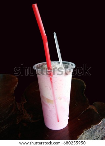 Closeup of cold milk pink with red straw and spoon in plastic cup on wooden table and black background 