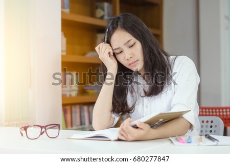 young girl student with homework and school concept - bored Asian girl student reading book or textbook of business, fail and stress startup business at the library