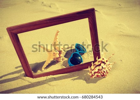 Summer photos concept. Frame on sand on the beach. Seashells and sunglasses lying on the seashore by the sea. 