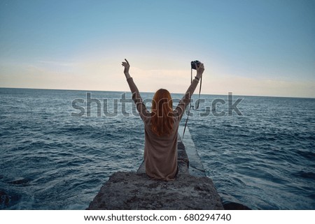 Woman is sitting on the dock looking at the sea and sunset                               