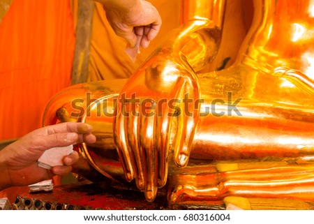 Ancient Buddha craftsman repairing cover with gold leaf.
