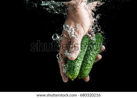A hand in the water holds cucumbers on a black background, washing vegetables before cooking and eating
