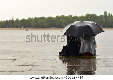 lovers sitting on quay under umbrella