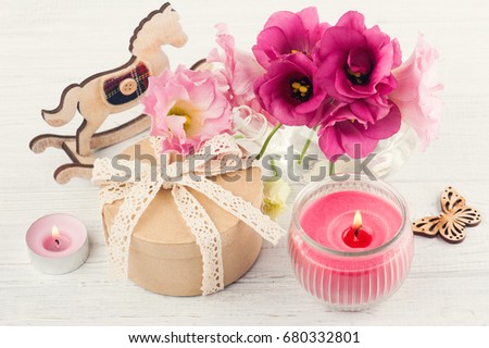 Hand crafted gift, lit candles, and red eustoma flowers on white wooden background