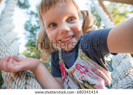 Joyful little girl with funny face, taking selfie in the park during playing. Blurred background, wide angle.