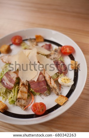 Cesar salad on white plate with black stripe on wooden background 