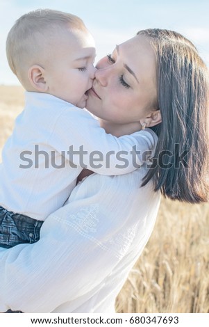 adorable baby boy kissing his pretty young mather outdoor at summer day. Family dressed in national white clothes