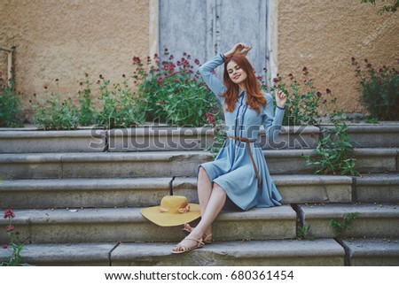 Woman in blue dress with hat on stairs on background of flowers, retro, vintage                               