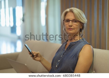 Portrait of businesswoman with smartphone sitting on sofa in office