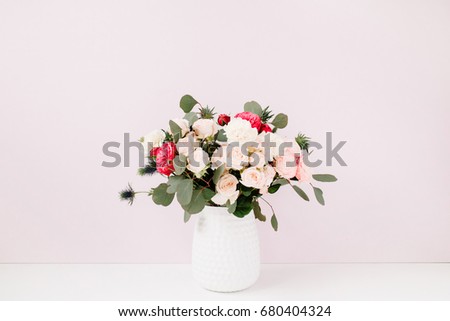 Beautiful flowers bouquet: bombastic roses, blue eringium, eucalyptus branches in flowerpot at pale pastel pink wall. Floral lifestyle composition.