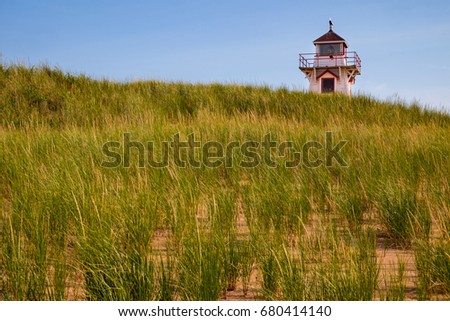Sand dune covered in grass with a lighthouse appearing over the top